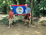 Susan and Hugh in front of the flag of the country of Belize Photo from Susan's Story, Susan and Hugh in front of the flag of the country of Belize